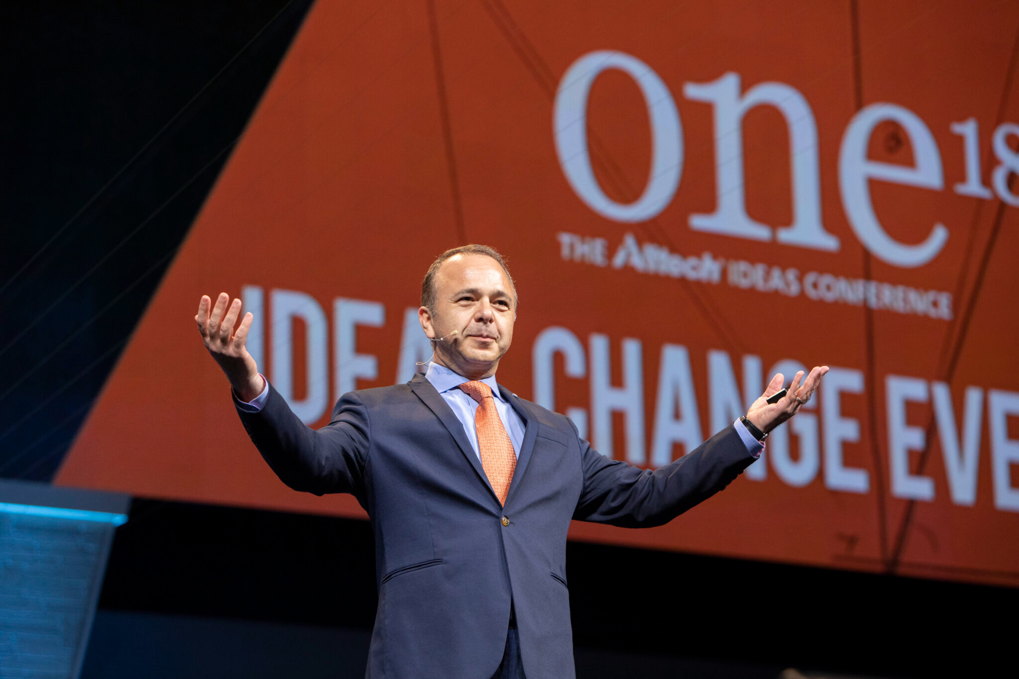 Dr. Fotuhi speaking at One18 conference, orange background visible.